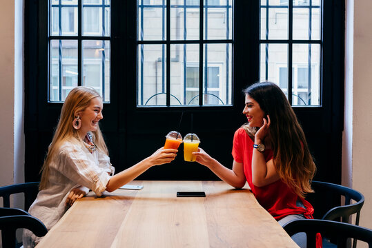Cheerful women clinking cups of juice in cafe