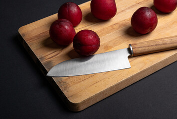 Red plums on bread board with knife and black background