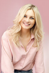 Blond woman in casual style. Girl in a shirt and with tousled hair. Blond woman in pink colors. Pastel colors and a girl. Girl smiles widely. Beautiful blonde and pink.