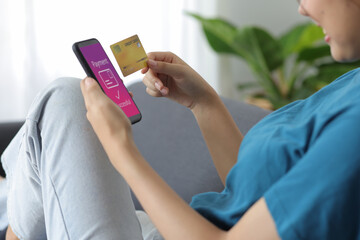 Cheerful Asian young woman lifestyle while sitting on sofa at home using mobile phone and having fun. Woman holding credit card and shopping online.