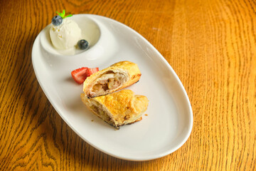 A piece of apple strudel with vanilla ice cream and strawberries