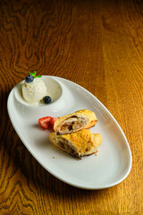 A piece of apple strudel with vanilla ice cream and strawberries