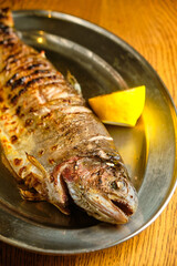 Fried fish lying on a black plate with vegetables and lemon