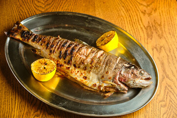 Fried fish lying on a black plate with vegetables and lemon