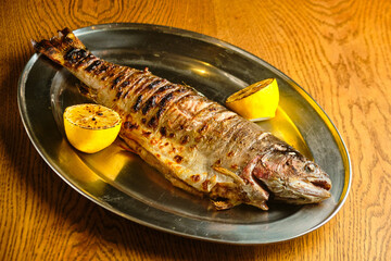Fried fish lying on a black plate with vegetables and lemon