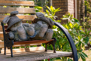Two puppets sitting alone on a bench outside in the garden patiently waiting