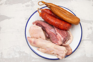 raw meat, pork ear and smoked sausages on white dish