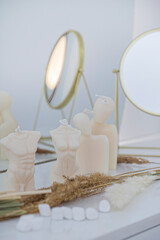 Body candles on the dressing table with spikelets of dried flowers, marshmallows and a mirror on a light background.