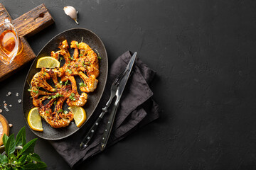 Vegetarian cauliflower steaks with microgreens and lemon on the black background, top view copy space for text. Alternative to traditional meat steaks for vegans.