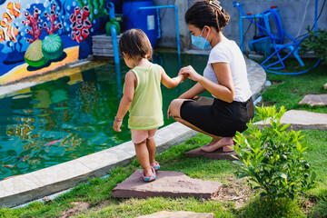 Naklejka premium Mother and son watching koi fish at the pond in the garden behind the house. The concept of relaxing family leisure activities.