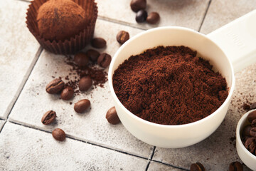 Coffee background. Measuring spoons with ground coffee, beans, cup and sweet chocolate truffles on old tile cracked table background. Food background. Top view with space for your text