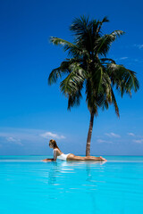 Elegant tanned woman in white swimsuit in pool on tropical Maldives island. Beautiful bikini body girl in pool with view on horizon. Sexy model near the pool on beautiful Indian ocean landscape.Travel