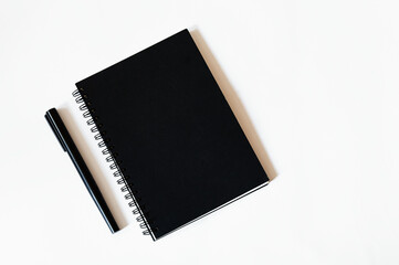 A notebook in a black cover and a black pen lie side by side on a white background, a minimalist composition, top view