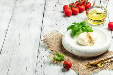 Creamy Italian Burrata Cheese with basil, olive oil and cherry tomatoes on white plate on light wooden background. banner, menu, recipe place for text, top view