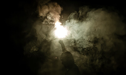 A man holds a hand flare with white smoke.