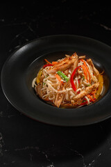 Pasta. udon noodles with Chicken and vegetables on a plate on black stone background.