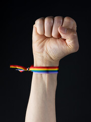 Raised fist with LGBT rainbow flag bracelet. Black background