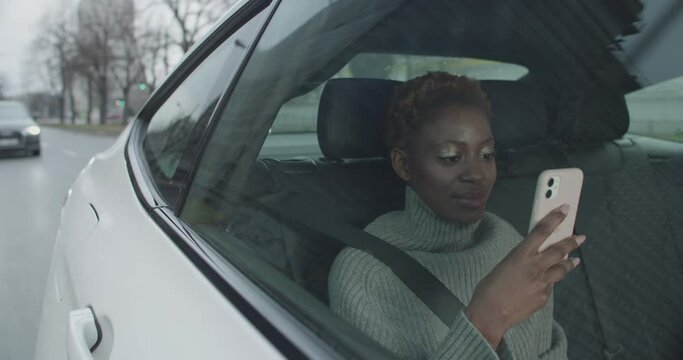 Young black woman car passenger is using her mobile phone while riding the uber
