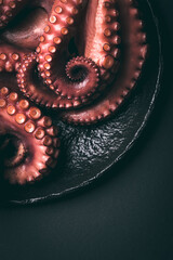 Octopus. Octopus tentacles on the dark volcanic dish on the black background, close-up, macro.  Aesthetic composition, dark key. Seafood ingredient in Japanese, Korean and Mediterranean cuisine