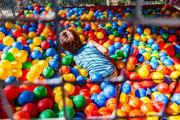 Fototapeta na wymiar A child plays in a ball pool filled with colorful plastic balls on a playground