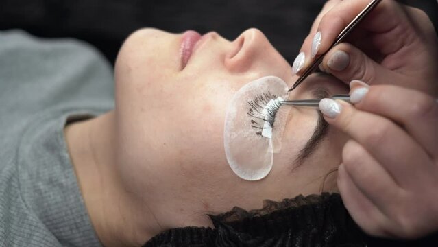 Eyelash extensions, fake eyelash extension procedure. Close-up portrait of a woman's eyes with long eyelashes in a beauty salon. Professional stylist lengthening female eyelashes