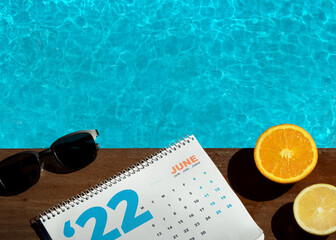 Top view of swimming pool with orange, lemon, sunglass and calendar. Summer time. Summer calendar. Summer 2022.