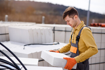  man contractor builder is holding an autoclaved aerated concrete block aac on a construction site.