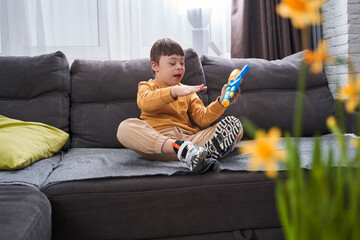 Little boy with Down syndrome sitting at the sofa with his toy gun while relaxing