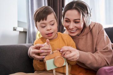 Cheerful woman sitting at the sofa and playing with her little son
