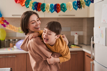 Boy with Down syndrome laughing out loud while his mother holding him