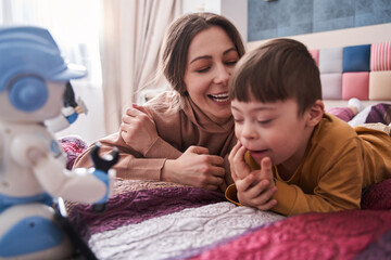 Caucasian woman laying at the bed and looking at her son with Down syndrome