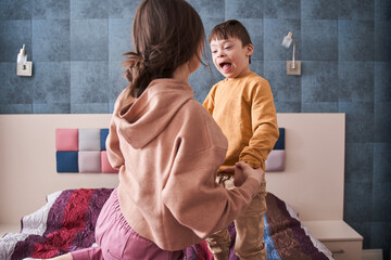 Mother and her son with Down syndrome playing at the bed at the bedroom
