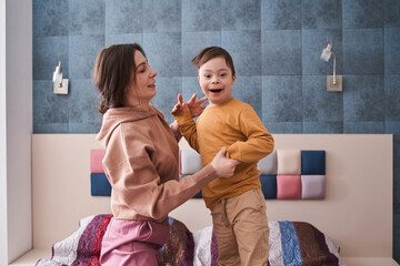 Boy with Down syndrome playing with his mother at the bed at the bedroom