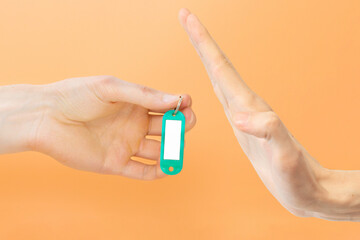 Man hand refusing a green key tag with space for text on a yellow background. Denial. Blank. Name....
