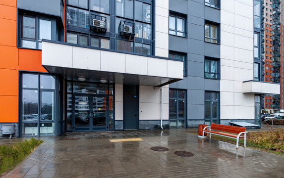 White, black, orange apartment building, view of entry with bench multi-family residential area wet rainy day
