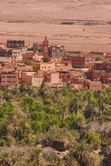Fototapeta na wymiar Earthen-clay old tradional kasbah with a palm trees plantation in the foreground. Moroccan landscape