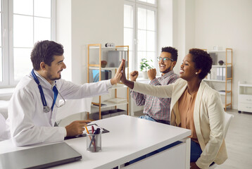 Fototapeta premium Smiling man doctor give high five to happy multiethnic couple at hospital consultation. Happy male GP celebrate successful pregnancy planning or good medical results with excited ethnic young family.