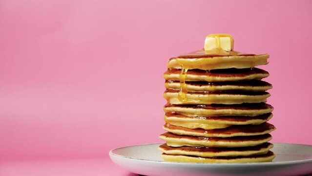 Pancakes with butter and poured honey or maple syrup moving on pink background. Close-up high quality 4k footage