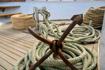 Rusty anchor with coiled rope lies on wooden deck of yacht. Auxiliary yacht equipment. Copy space. Close-up. Selective focus.