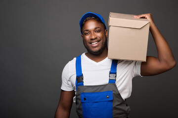 Against gray background, strong black guy confidently holds cardboard box with office supplies on...