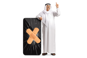 Man in ethnic clothes leaning on a big smartphone with a bandage strip and pointing up