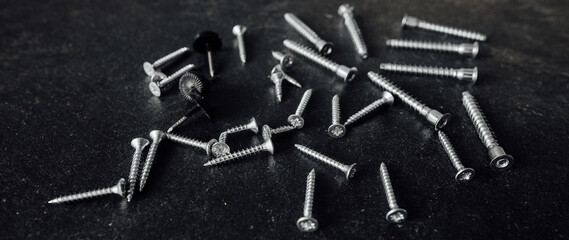 A bunch of self-tapping screws on the table. On a dark background.