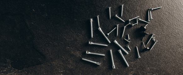 A bunch of self-tapping screws on the table. On a dark background.