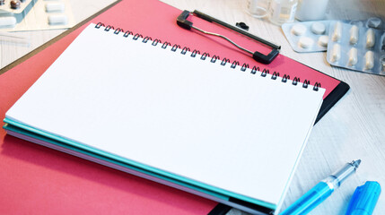 Medical desktop with a white notepad on red folder with pilss and pen. Workplace of a doctor. Top view on doctor's table with medical equipment. Medicine and health concept