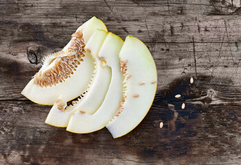 Slices of sliced melon with seeds and skin on a wooden countertop.