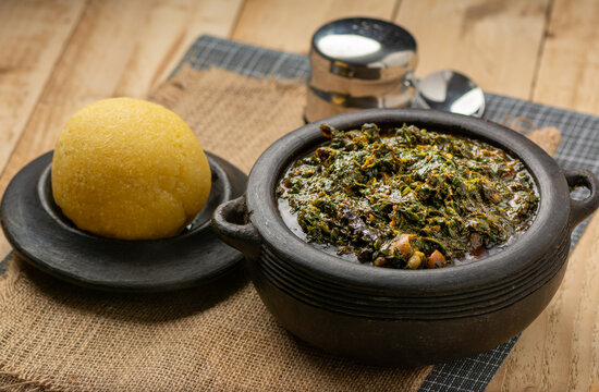Efik Afang soup served in a clay bowl with garri on a wooden background