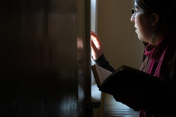 Woman looking out a window with Bible in hand