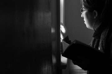 Woman with Bible looking out window (black and white)