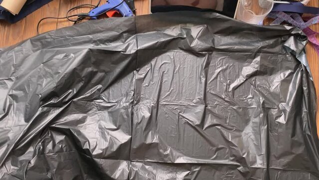 Women's hands spread garbage bag on wooden table and pick up styrofoam Celtic axe. Workshop of cosplayer. Diy craft made of foamed polyethylene. Viking hatchet for medieval fighting festival.