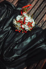 wedding decor. informal wedding bouquet white flowers with red berries on the black leather jacket on bench background at sunny day. wedding concept, free space